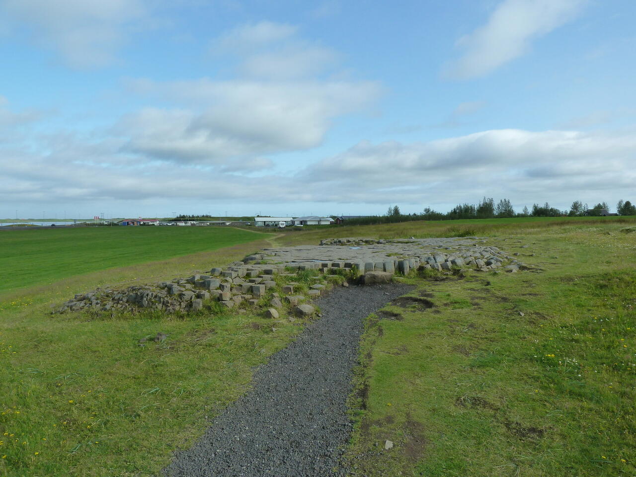 Kirkjugárd aus der Ferne, eine etwas erhabene Plattform aus Steinen inmitten von Feldern; (c) Stephan Matthiesen 2011