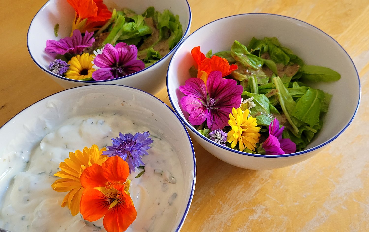 drei weiße Schüsseln mit Salat und Kräuterquark, mit bunten Blüten dekoriert